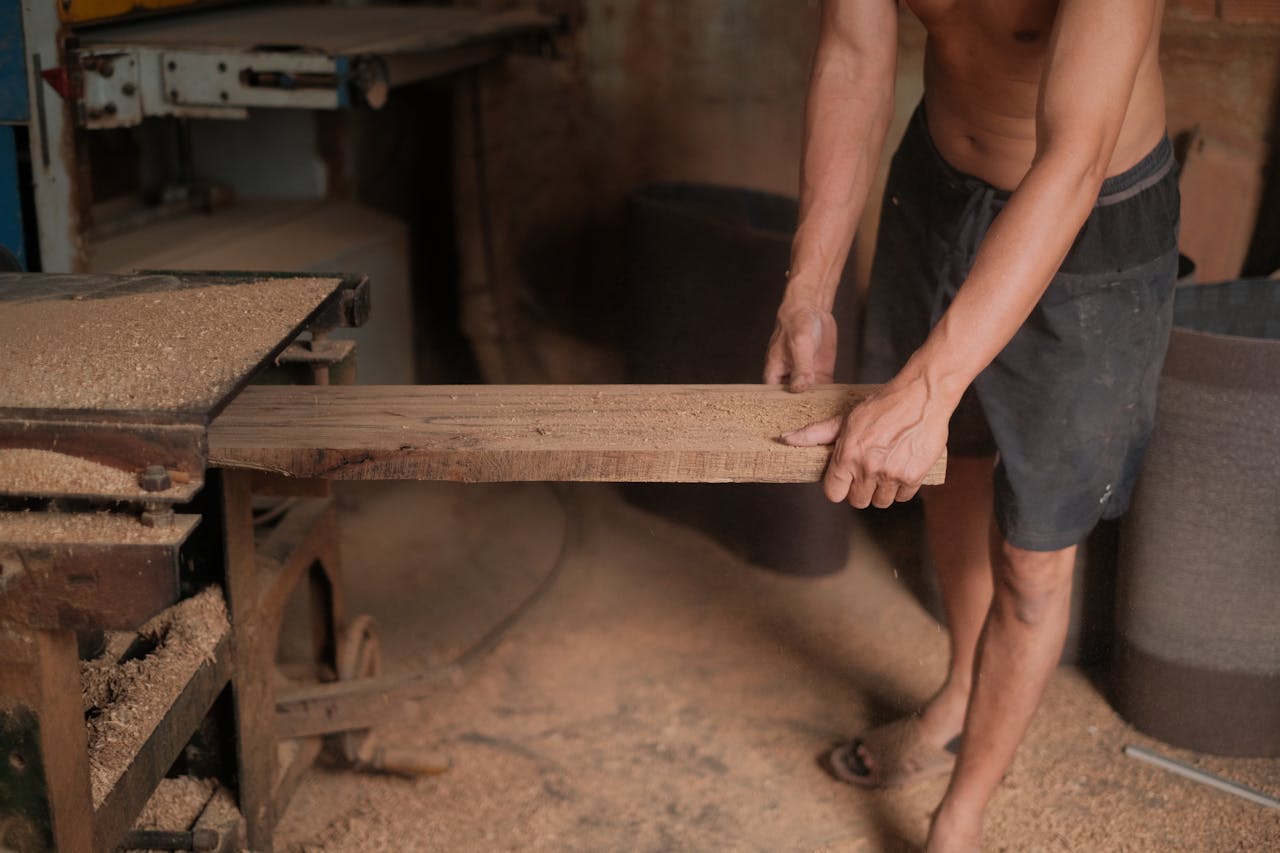 A man processing a wooden plank using a sanding machine in a workshop.